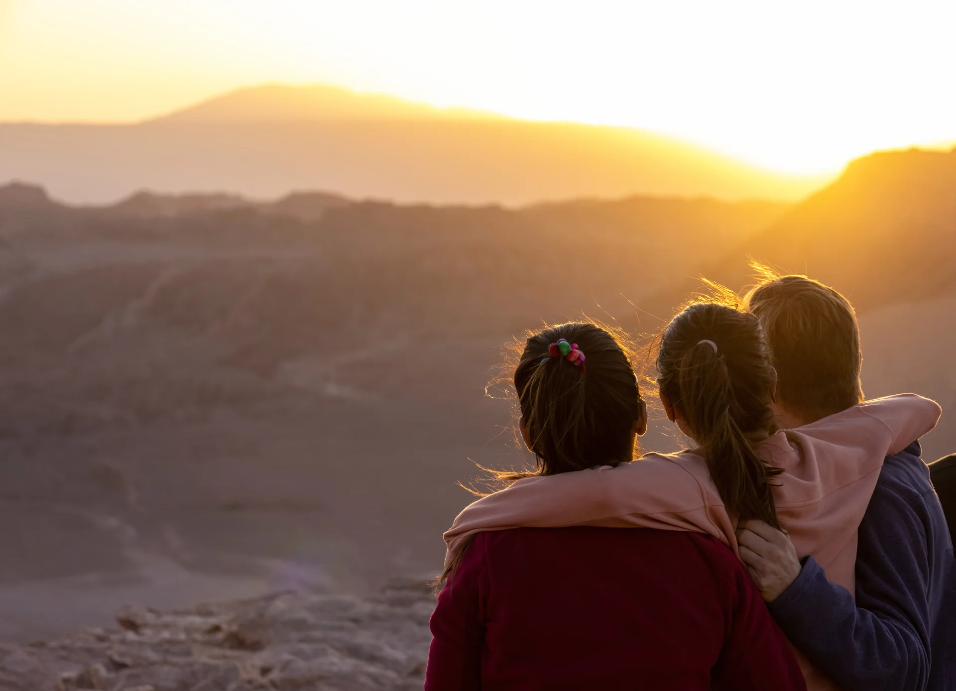 Tres personas abrazadas observando la luz del atardecer desde el mirador de Ckari