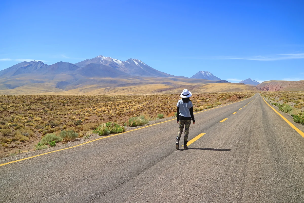 Viajera caminando por una carretera del desierto de Atacama hacia el paisaje cordillerano